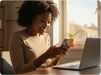a woman sitting in front of her laptop while holding her phone. 